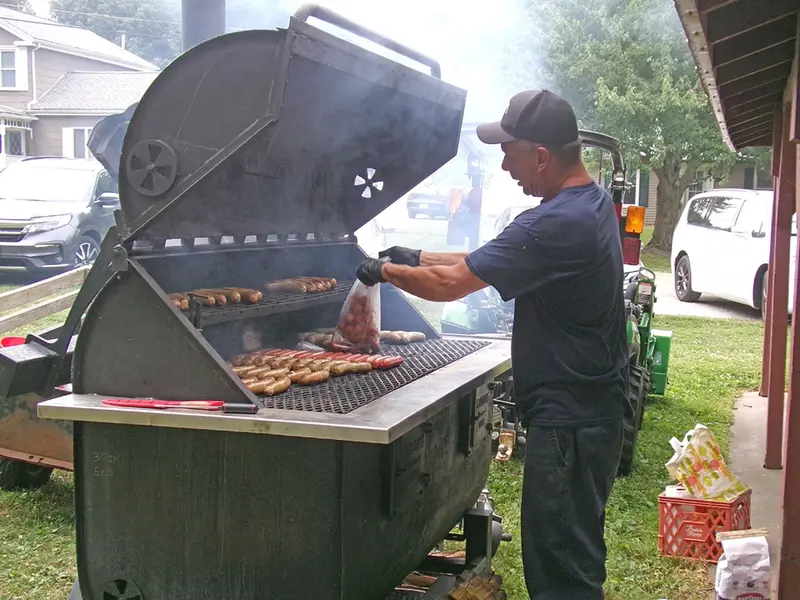 Grill master John Larimore loads the grill with hot dogs.