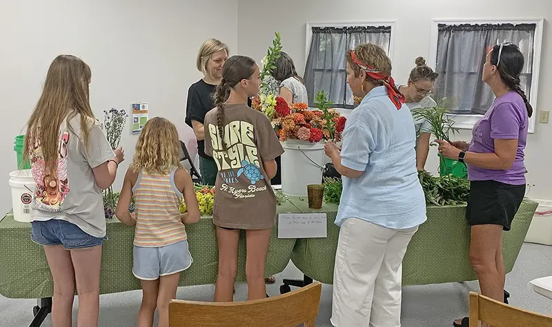 From Stem to Style — (Left to right) Lauren Bond, Lainey Bond, Cassidy Griffith, Tori Noreuil, instructor Sarah Flint, Kelly Watts, Natalie Lessen, and Michelle Noreuil gather blooms at the Ayer Library’s flower arranging workshop, kicking off a class in color, creativity, and community.