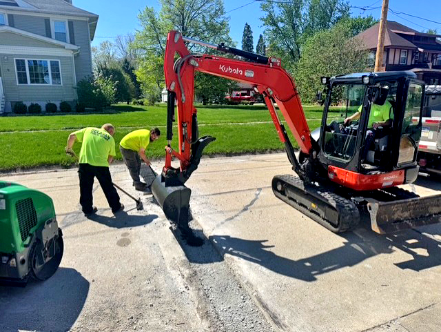 Eric Pemble and Gage Galloway smooth and level the fresh asphalt as Nathan Barnett deposits material into the cut joints along East 3rd Street.