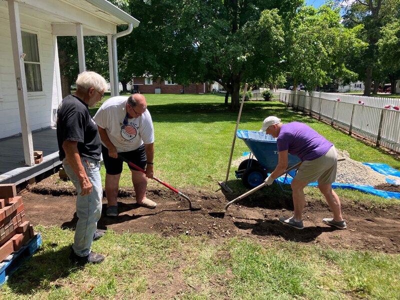 Delavan Historical Society members Jerry Engel (left), Mark Cunningham (center) and Mary Ruth Lowry (right) work together to prepare the pathway for brick installation along the sidewalk leading up to the Colony House.
