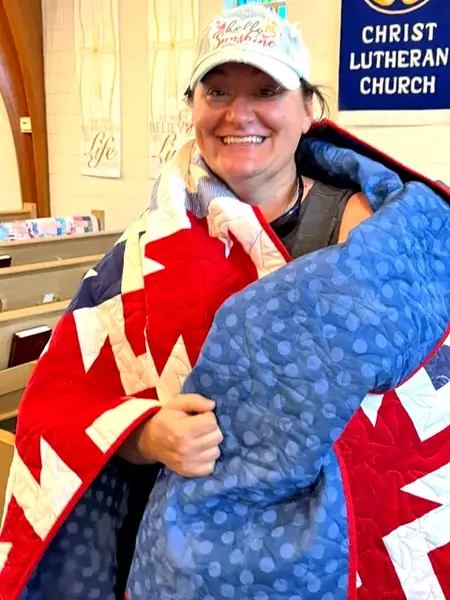 Brittany Thousand wraps herself in the handmade quilt presented by the Delavan Quilt Guild during the Fall Festival quilt show at Christ Lutheran Church. Guild members surprised the veteran and new Delavan resident with the gift in appreciation of her military service.
